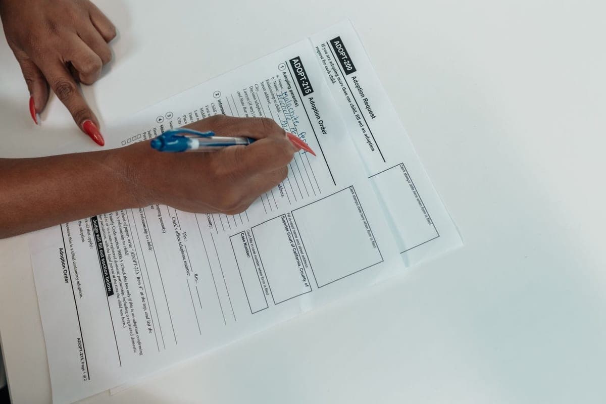 A hand filling in a printed paper form by hand with a ballpoint pen.